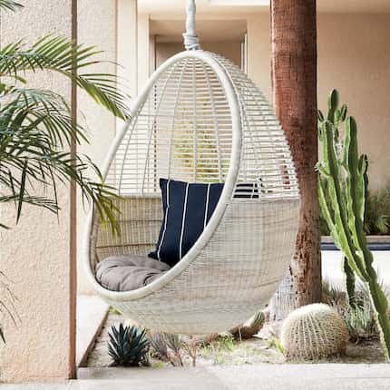 A white hanging chair with cactus in the background.