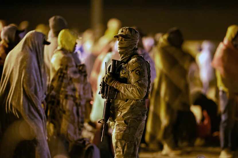 A Texas National Guard soldier provides security around migrants gathered around a gate in...