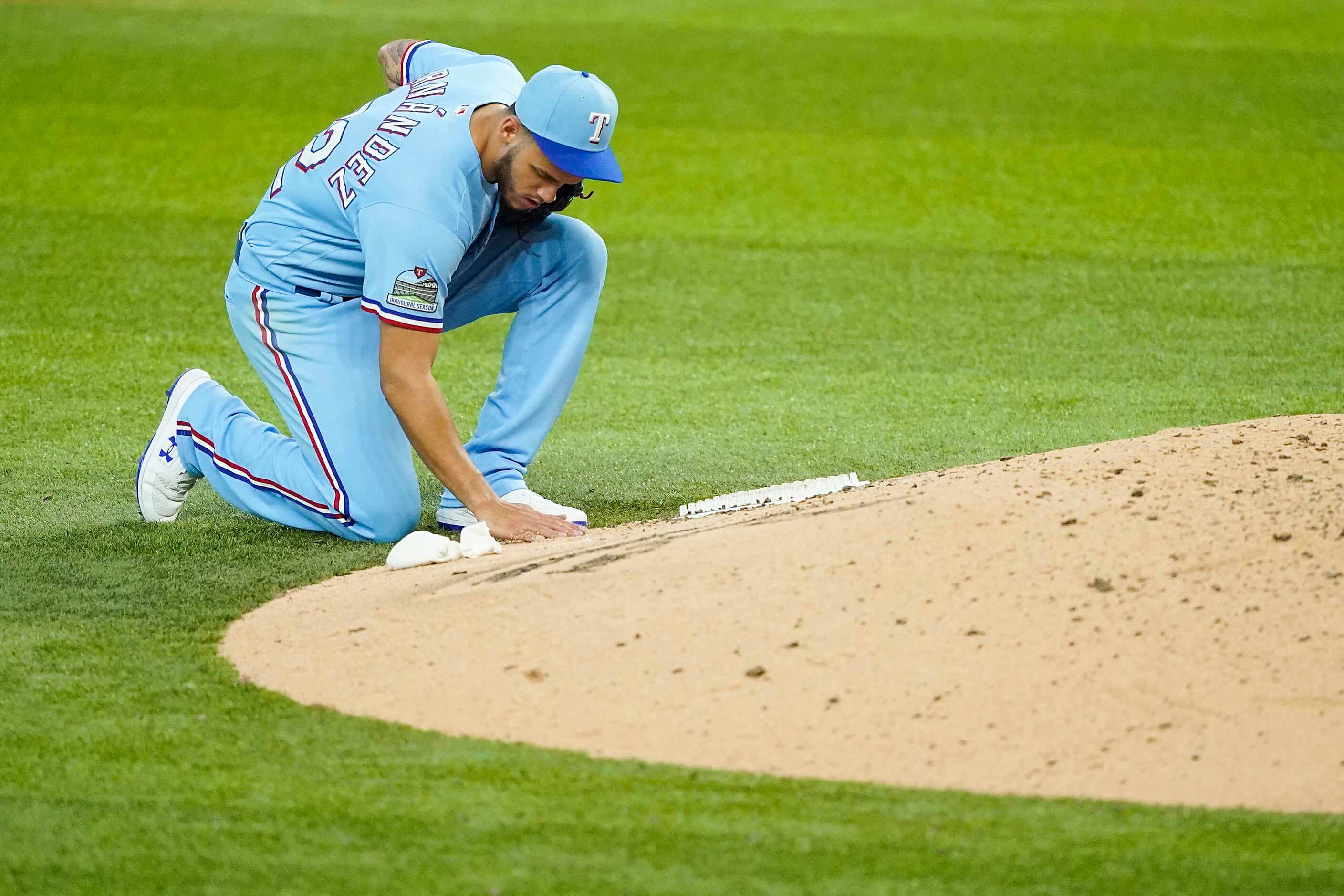 Texas Rangers pitcher Jonathan Hernandez writes in the dirt at the back of the mound as he...