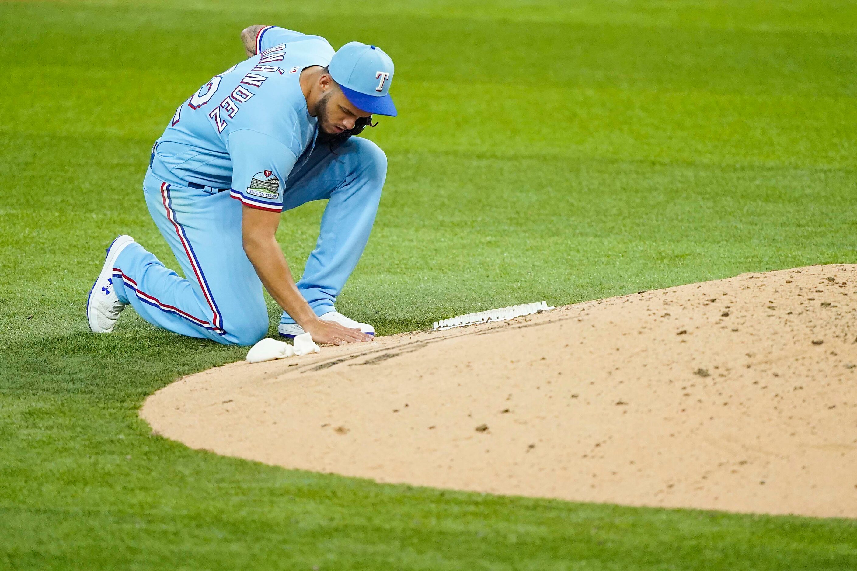 Texas Rangers pitcher Jonathan Hernandez writes in the dirt at the back of the mound as he...