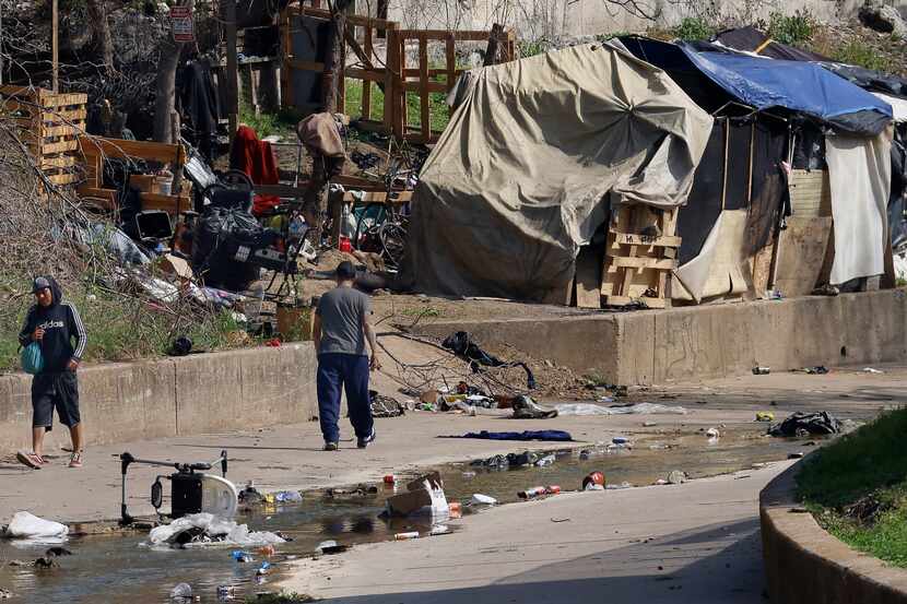 Men come and go Tuesday from an encampment built along a concrete drainage culvert in the...