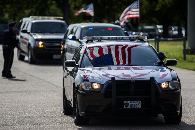 An American flag is reflected on a police car as officers arrive for a funeral service for...
