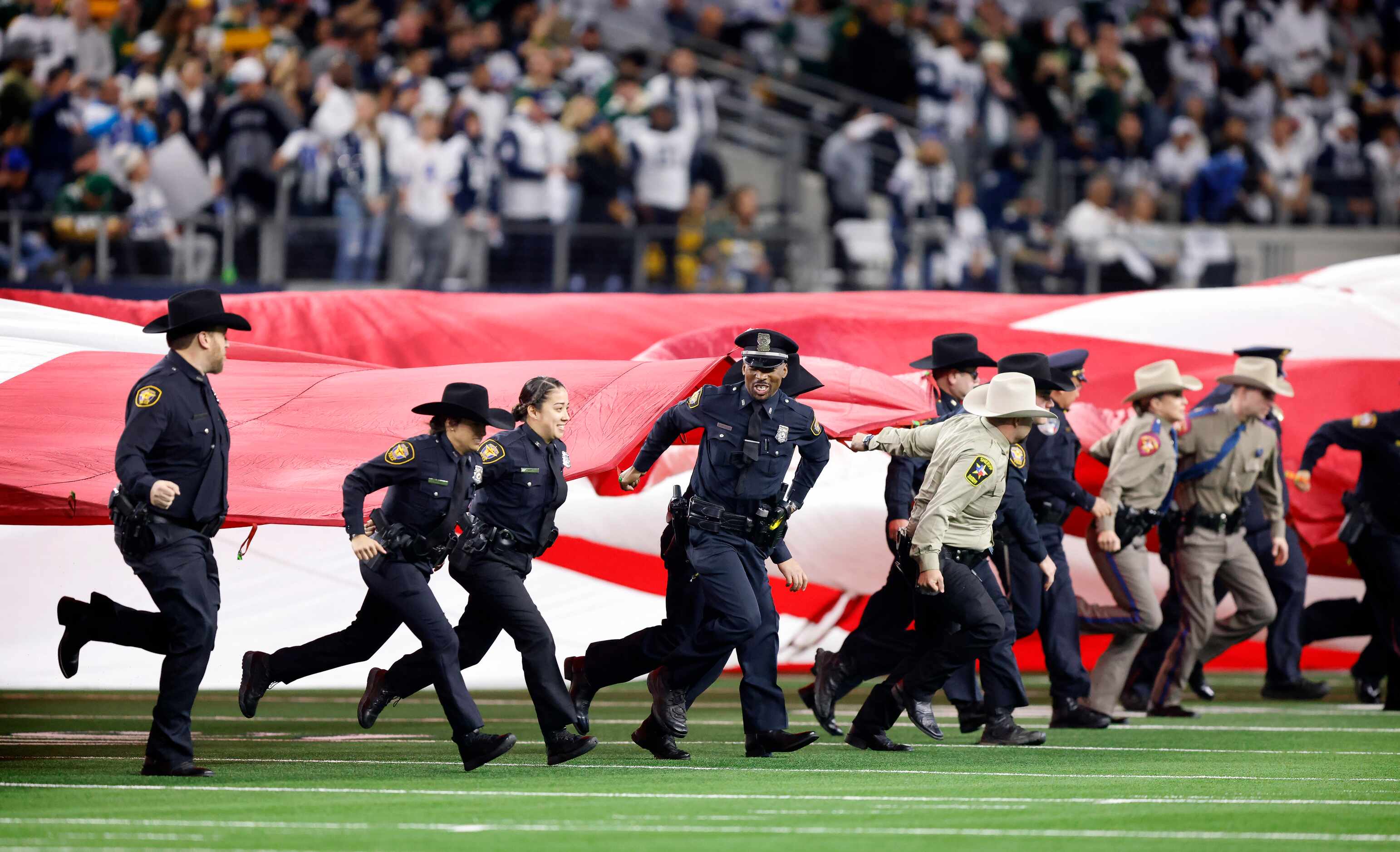 Law enforcement officers run with a field-sized U.S. flag as they spread it out for the...