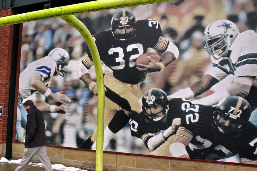 A pedestrian walks by a large photo, featuring Franco Harris (32) in action from Super Bowl...