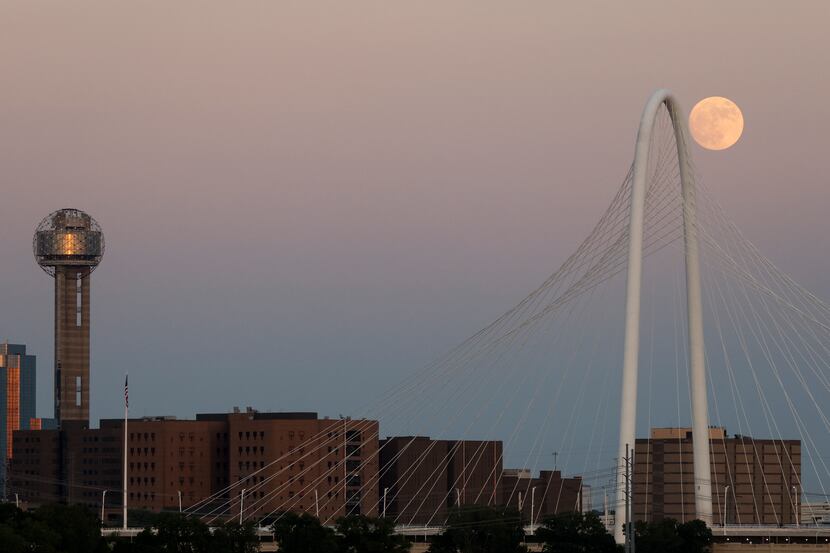 The moon rises next to the Margaret Hunt Hill Bridge and Reunion Tower on Tuesday.