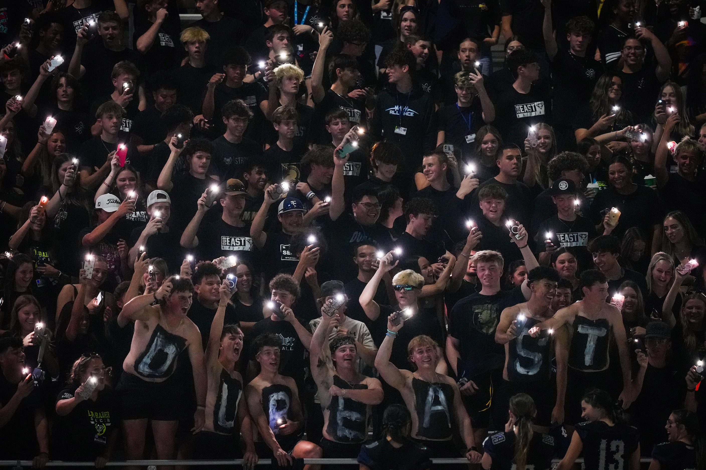 Wylie East students cheer their team while holding up their phone lights during the first...