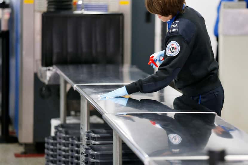 A TSA agent wipes down a table at a security checkpoint in Terminal C at DFW International...