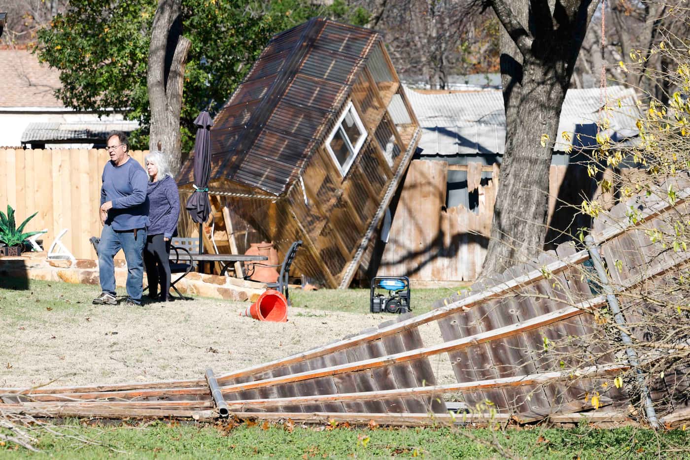 Homeowner Randy Popiel, front, walks by a damaged greenhouse sitting on the fence in the...
