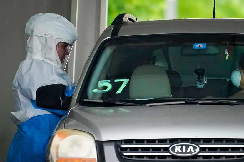 A healthcare worker screens the passenger of a vehicle at a Dallas County drive-thru...