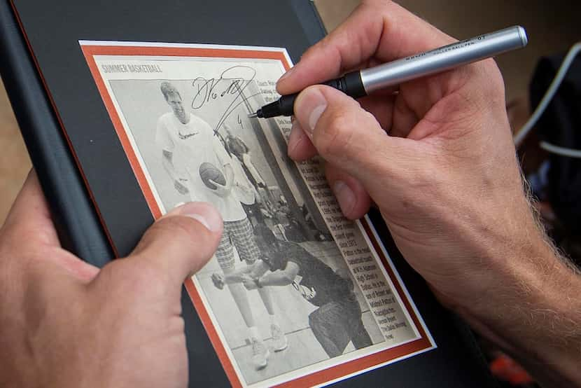 Dirk Nowitzki of the Dallas Mavericks autographs a newspaper clipping of himself with coach...