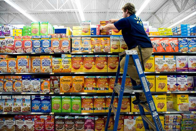 Wes Stevenson, a Walmart Academy student, climbs a ladder to perfect the cereal display in...
