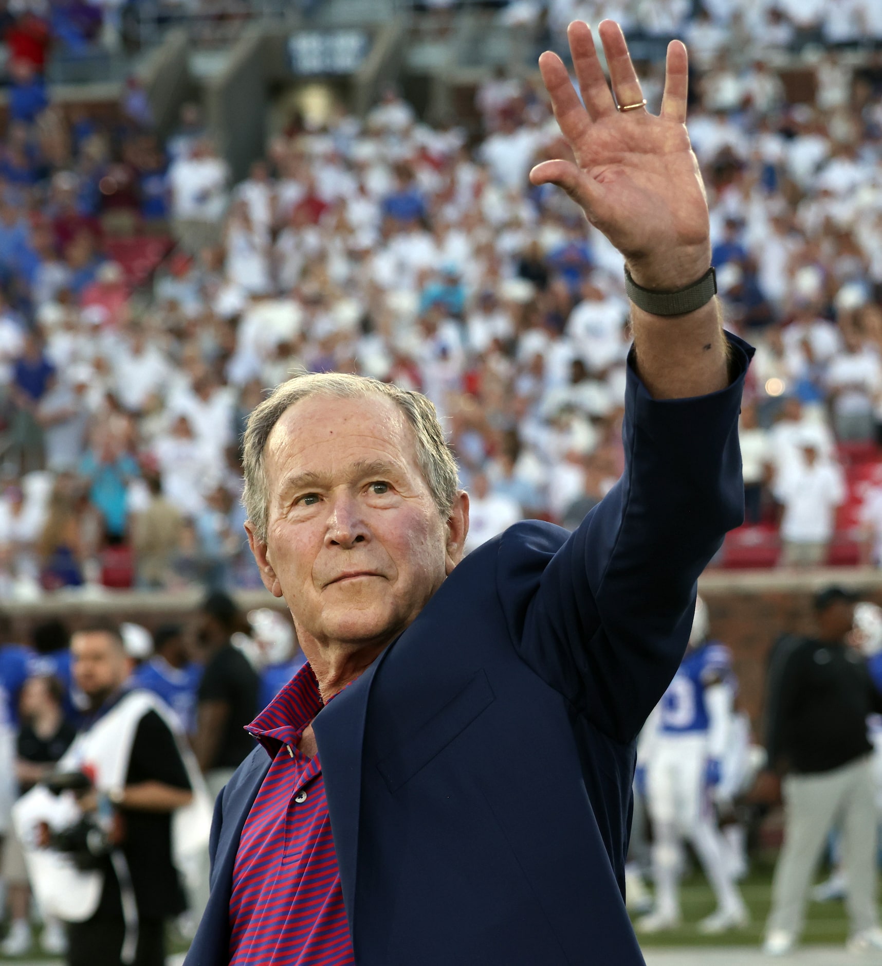 Former President George W. Bush waves to fans in the crowd on his way to midfield to flip...