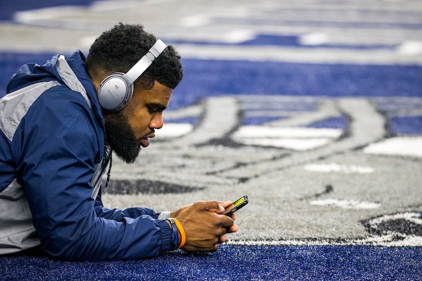 Dallas Cowboys running back Ezekiel Elliott looks at his phone as he stretches before an NFC...