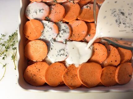 Pour a mixture of cream and fresh thyme over sliced seasoned sweet potatoes to make a...