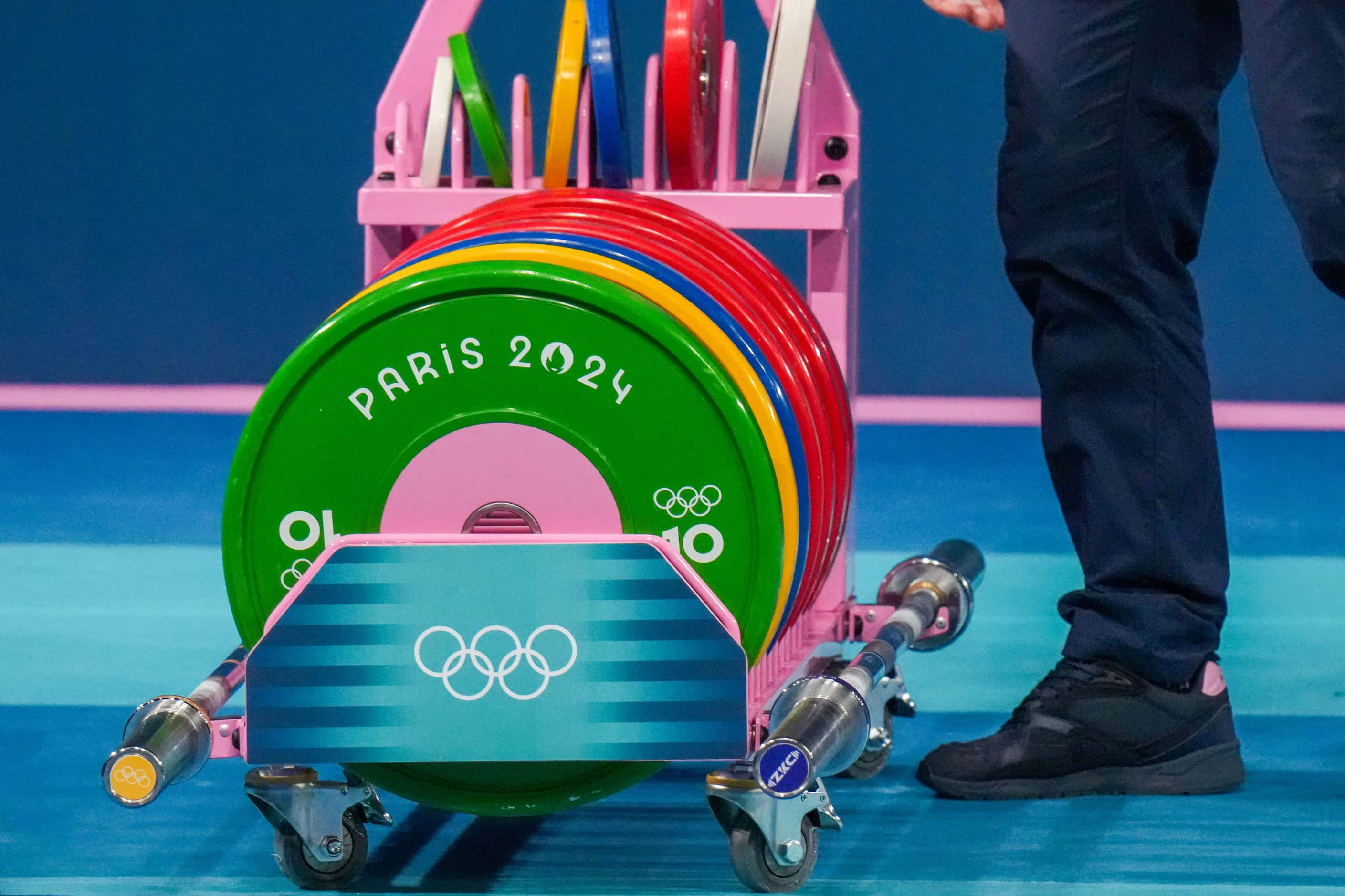 Workers reset racks of weights during women’s 49kg weightlifting at the 2024 Summer Olympics...