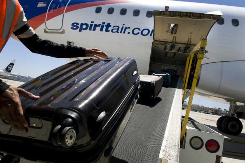 A ground crew worker loads a rolling bag onto a Spirit Airlines plane. Spirit is now...