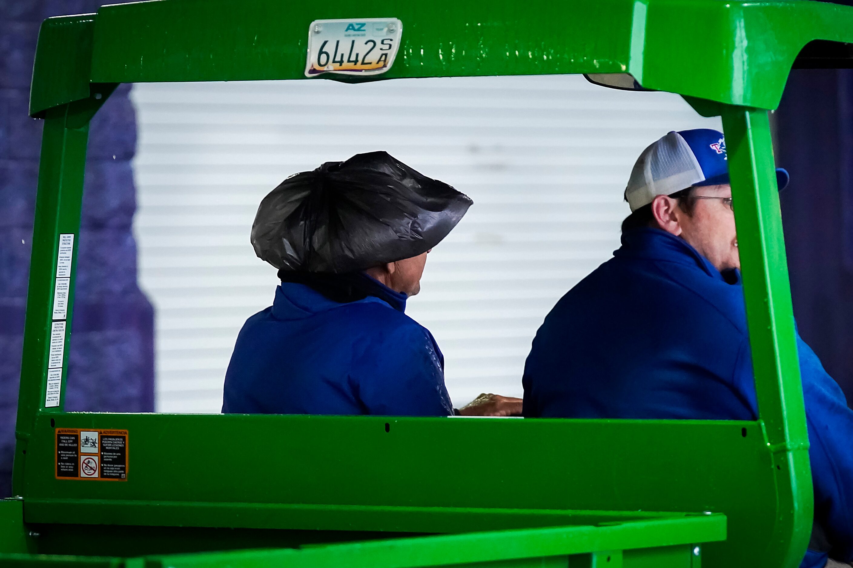 A stadium worker drives a cart with his hat coverd with a garbage bag as rain falls at...