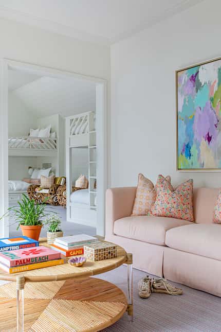 Pale pink sofa with patterned pillows sits behind a round table, off a bedroom with bunk beds