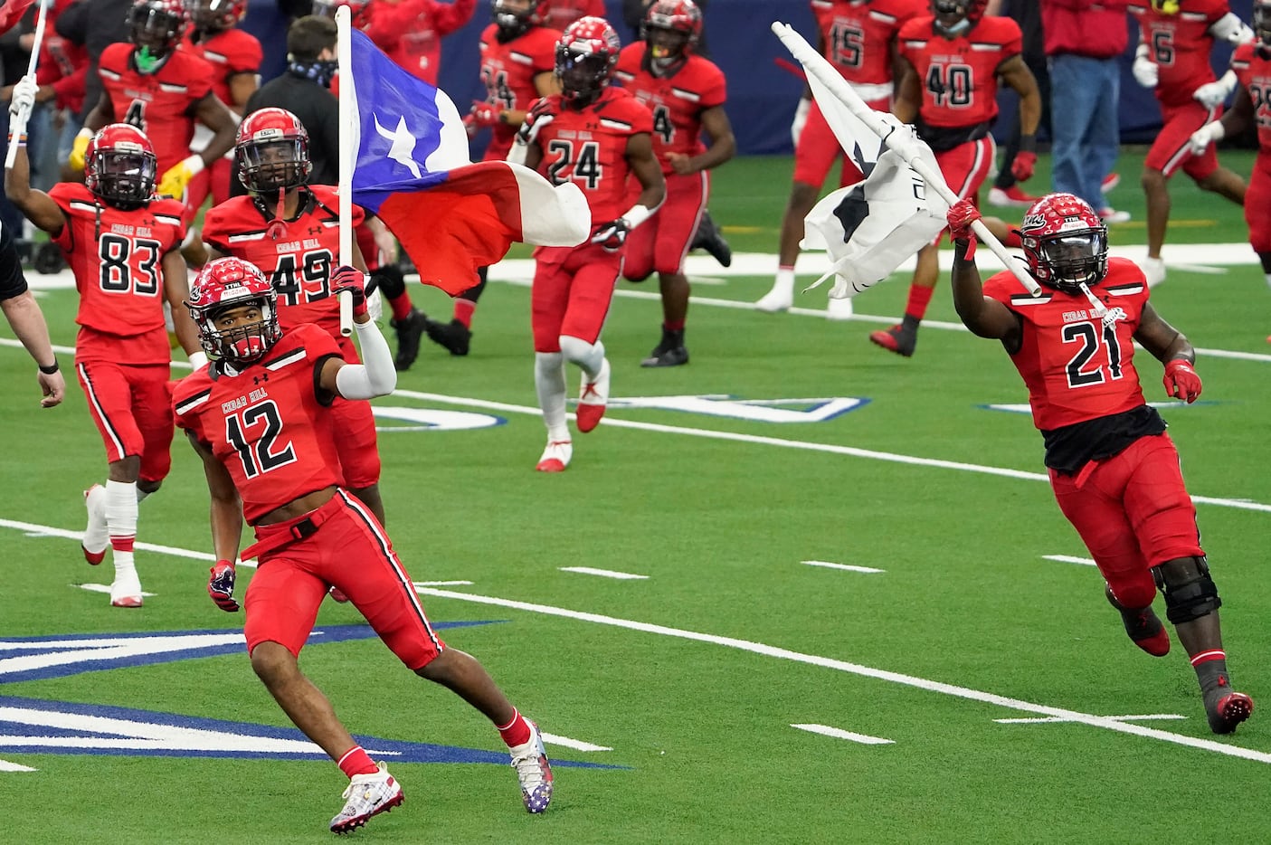 Cedar Hill’s Brian Rainey (12) and Kris Allen (21) carry flags as they lead their team on to...