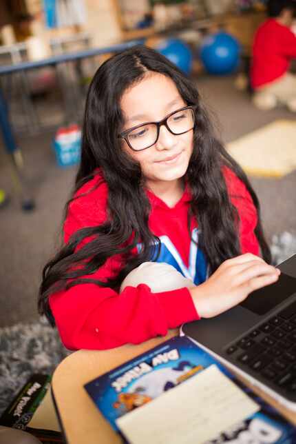 A young girl in glasses and red sweater completes an assignment online.