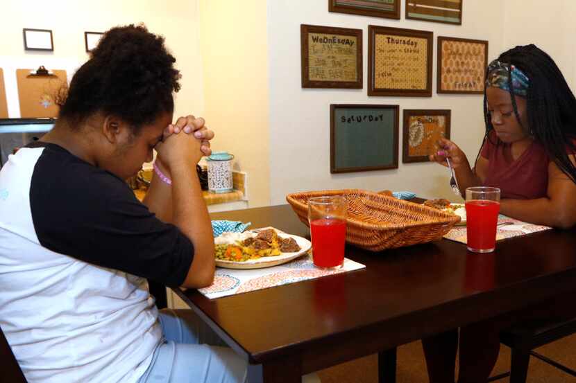 Amaris Dobbins, 13, prays before eating dinner with her mother, Ebony Green, in their...