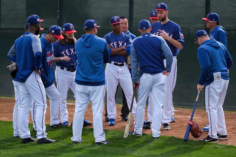 Texas Rangers manager Chris Woodward (leaning on bat) listens to pitcher Chris Martin speak...