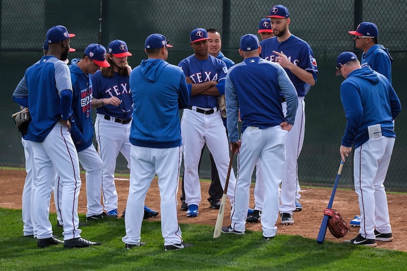 Texas Rangers manager Chris Woodward (leaning on bat) listens to pitcher Chris Martin speak...