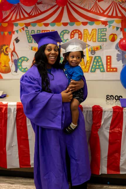 African American women in a graduation cap and gown poses with her toddler.