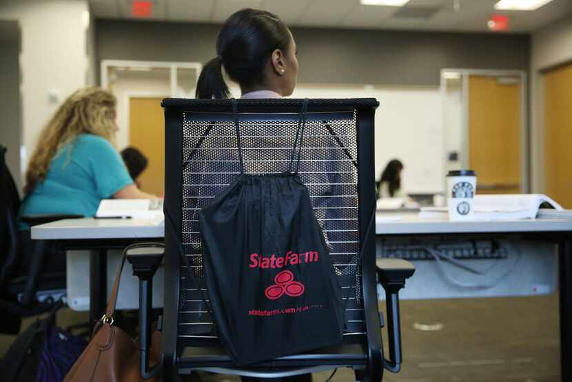 A State Farm backpack sits on a chair while students listen to an instructor during a...