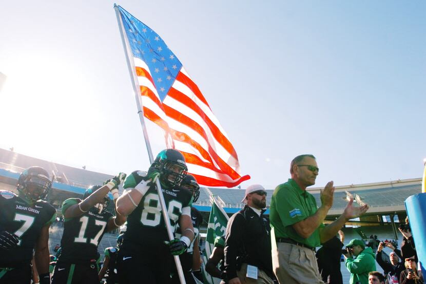 Led by senior tight end Drew Miller (86) holding the Stars and Stripes and head coach Dan...