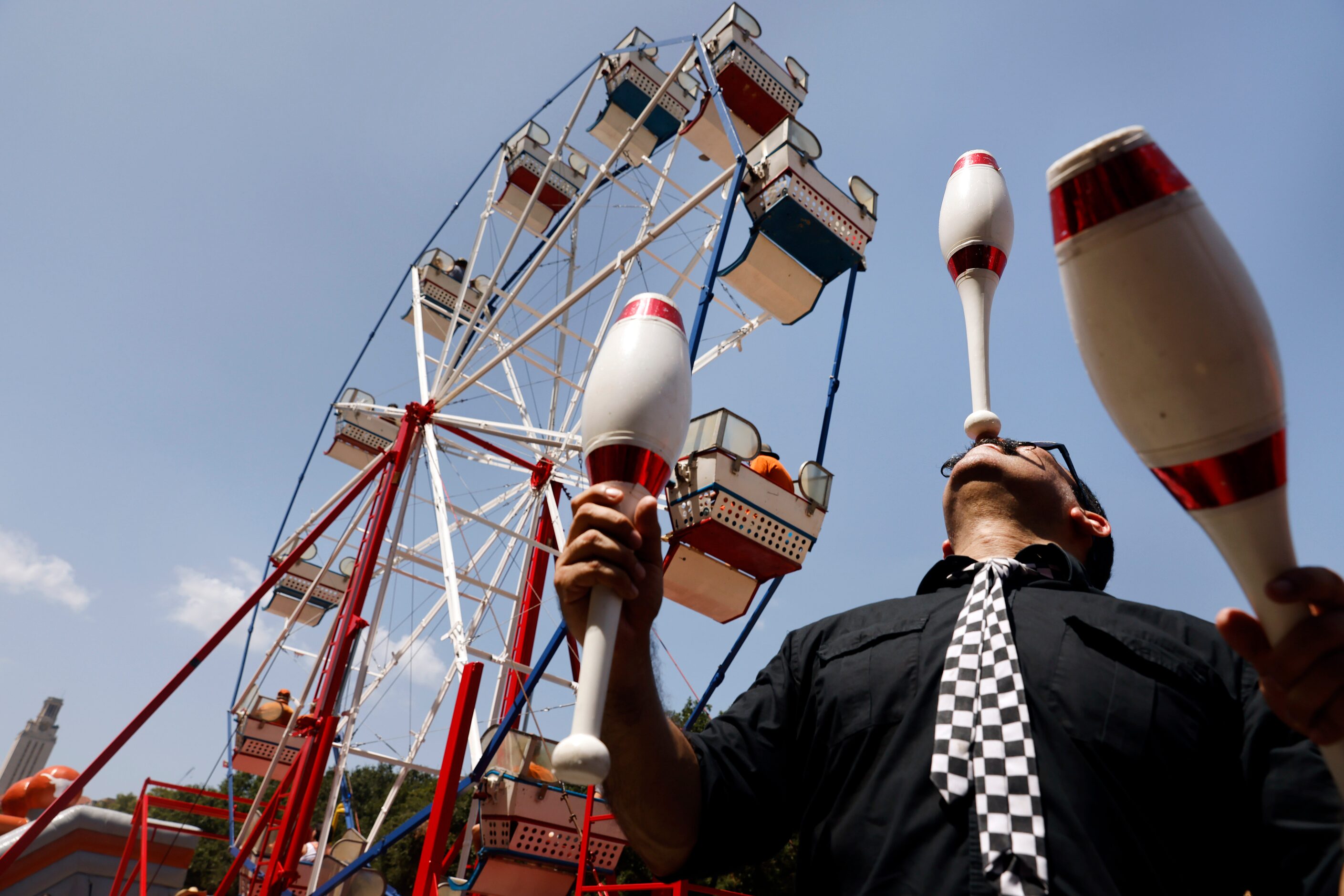 Circus performer Oscar Liendo juggles and glances bowling pins along Smokey's Midway outside...