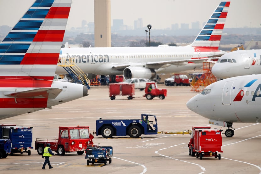 American Airlines crew members move luggage about as an aircraft is pushed back from the...