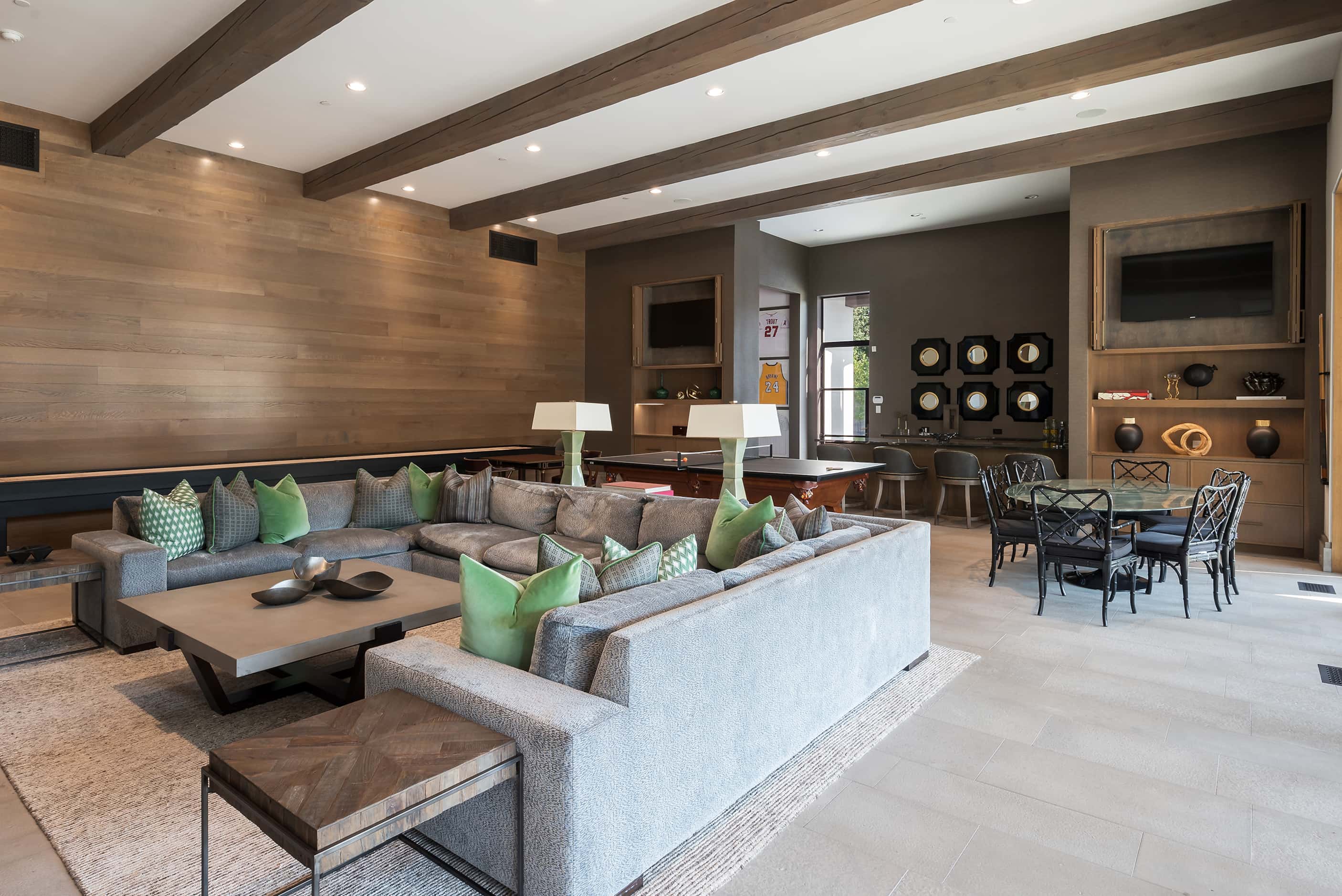 A game room has a U-shaped sofa, multiple game tables and a wet bar in the background.