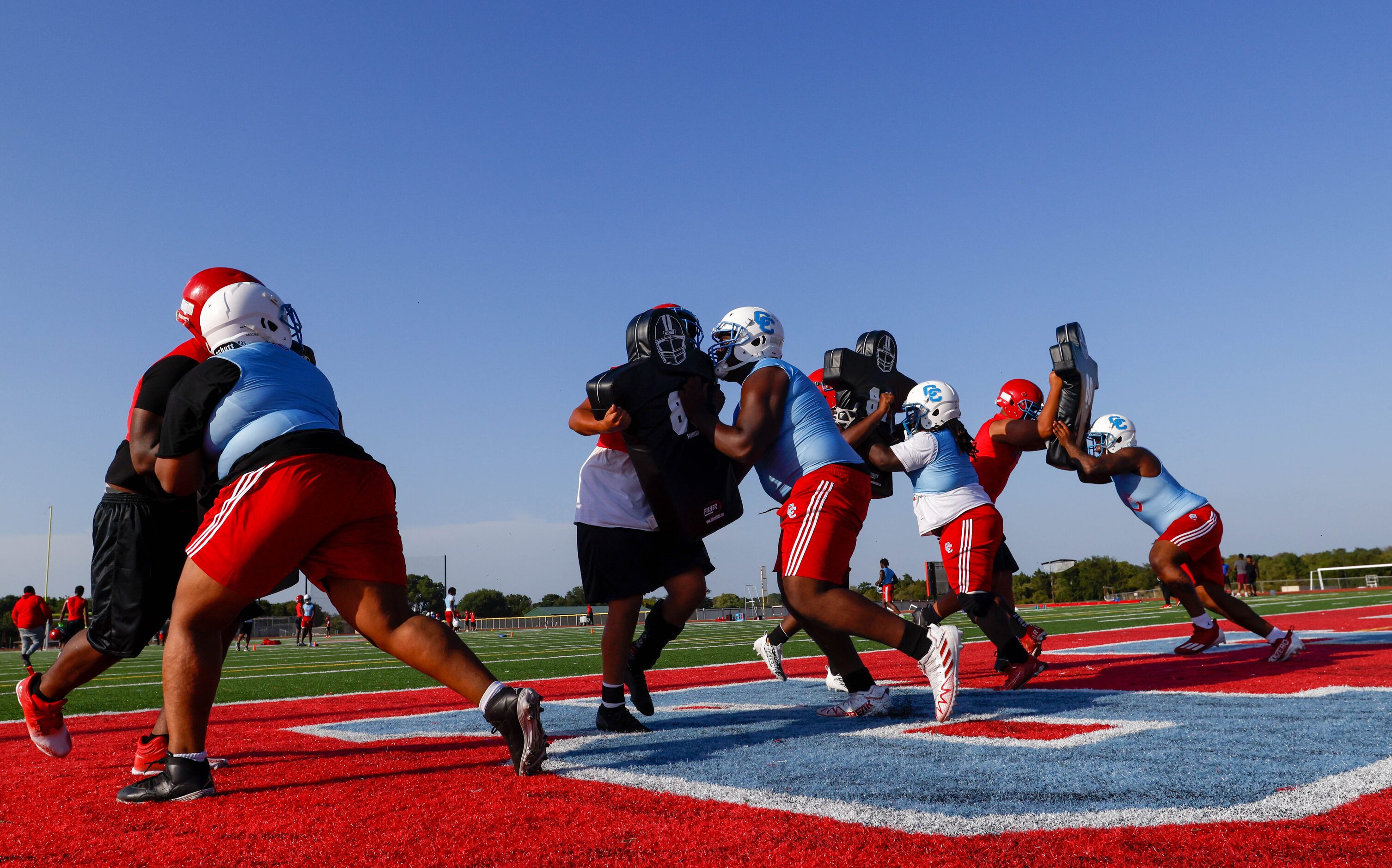 Members of the offensive line push against dummies held by teammates as part of a drill...