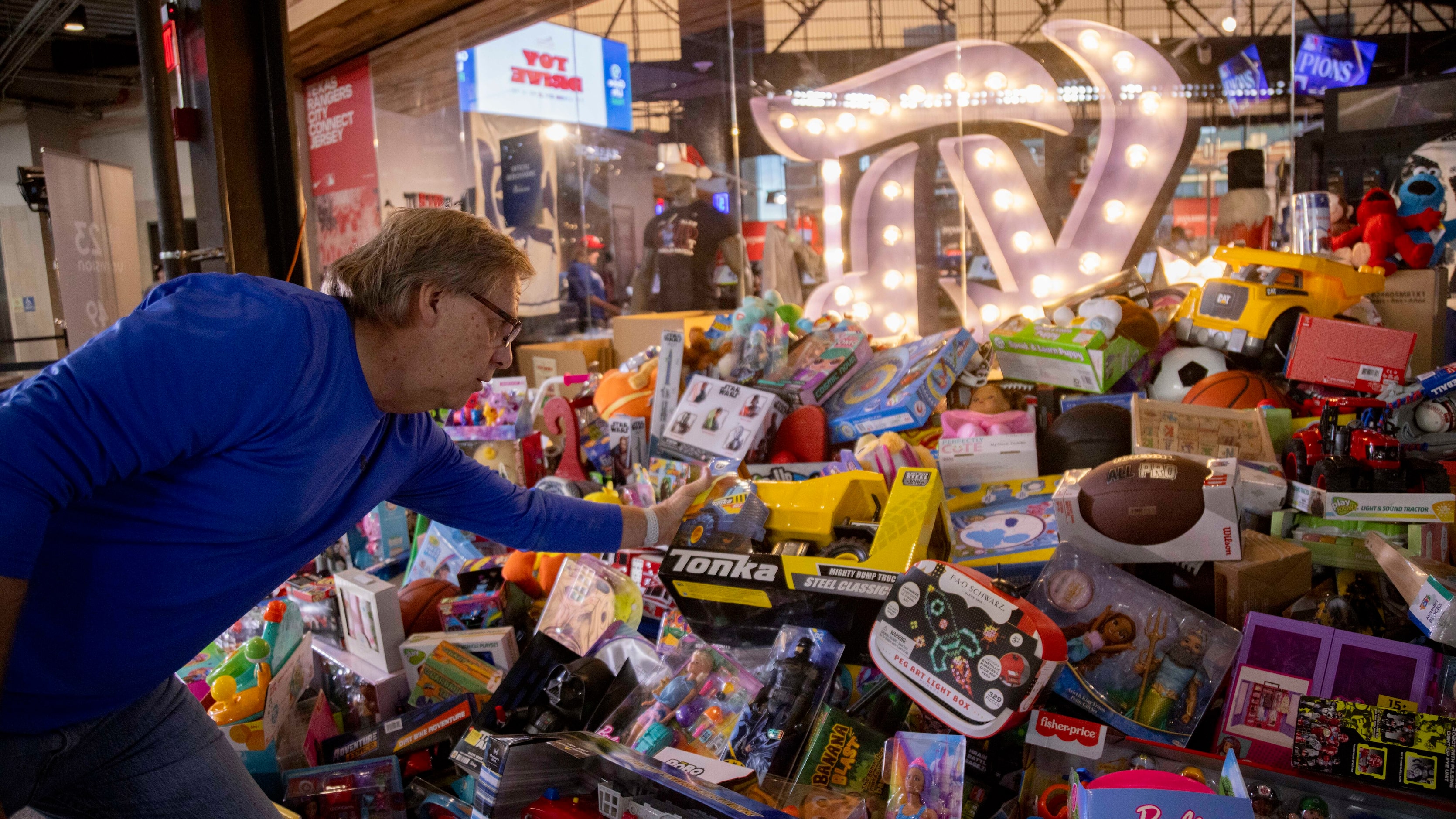 Volunteer Gary Avischious places a Tonka truck in the gift pile during the Texas Rangers Toy...