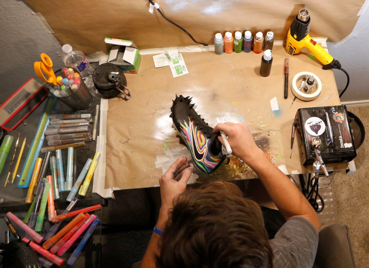 Luke Savage, 16, creates his art on a pair of cleats for SportsDayHS in his home in Dallas...