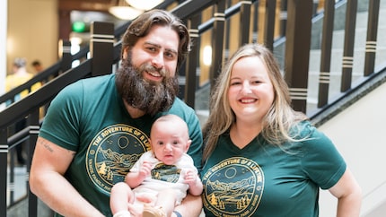 A bearded man stands with a blonde woman, both in matching green t-shirts, holding their...