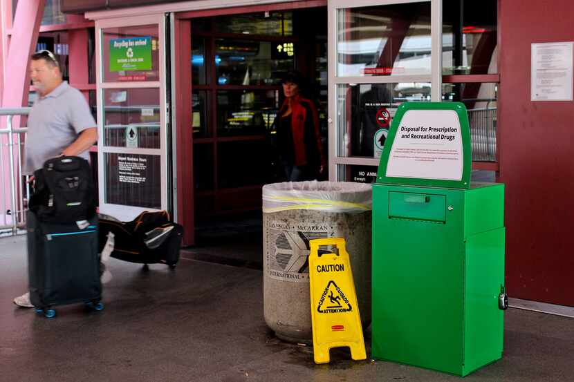 Unidentified travelers exit the airport past a green metal container designed for "Disposal...