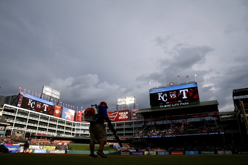 Members of the Rangers ground crew work to dry the field in a rain delay prior to the Kansas...