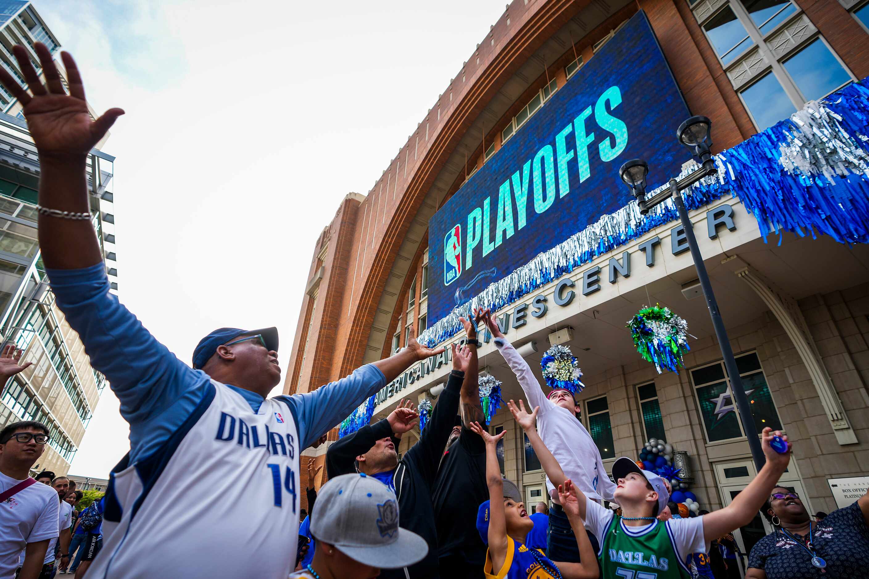 Dallas Mavericks fans reach for beads tossed to the crowd on the plaza before Game 3 of the...