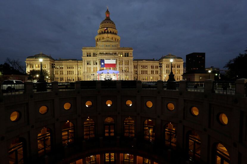 A large Texas flag hangs from the Texas State Capitol as workers prepare the grounds for...