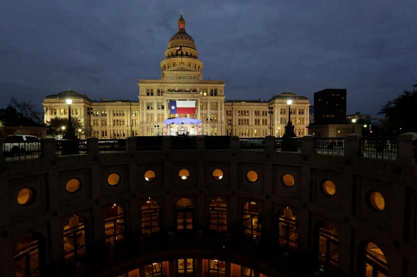 A large Texas flag hangs from the Texas State Capitol as workers prepare the grounds for...