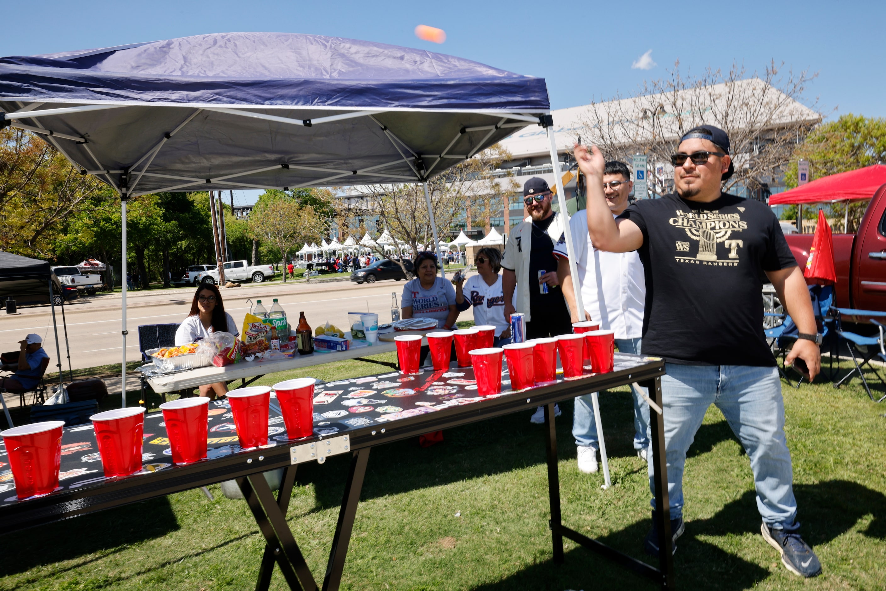 Texas Rangers fan Enrique Adame of Irving, right, throws a ball while tailgating with his...