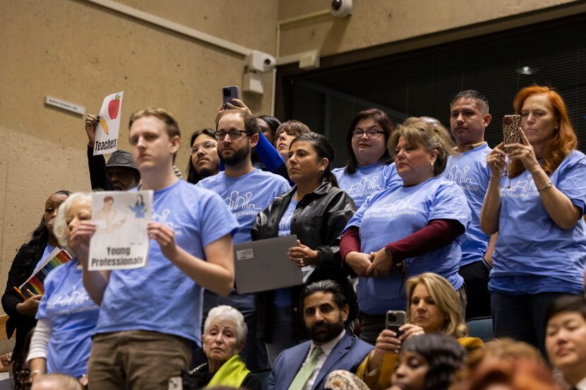 Community members with the Dallas Housing Coalition stand up as a speaker presents them...