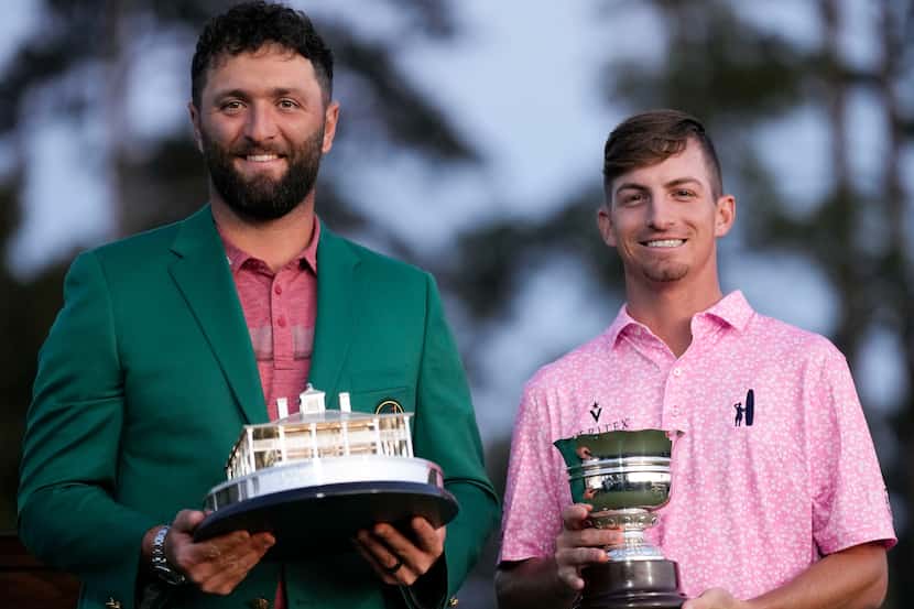 Jon Rahm, of Spain, holds up the Masters trophy as Sam Bennett holds the low amateur trophy...