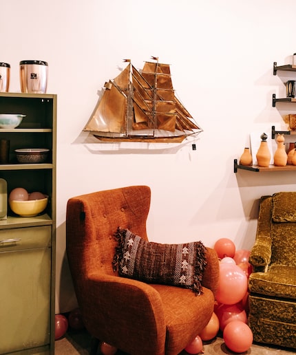 Vintage tufted chair with pillow and a brass ship decor piece on the wall.