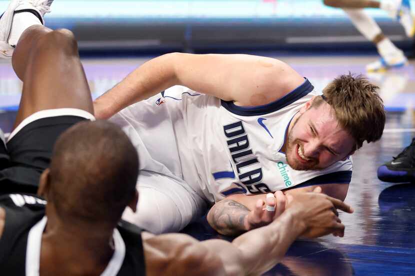 Dallas Mavericks guard Luka Doncic (77) winces as he goes to the floor after colliding on a...