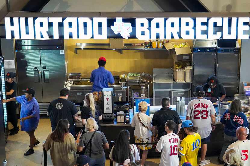 Customers wait in line for the Hurtado BBQ stand at Globe Life Field before a game between...