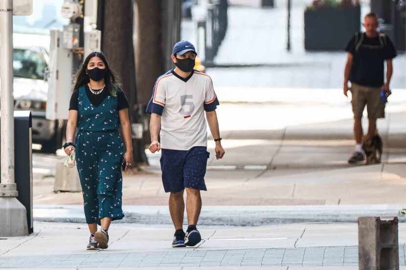 A couple of people wearing masks walk the streets of downtown Dallas on Wednesday, July 21,...