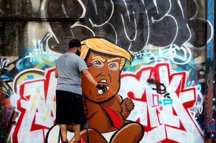 Dallas artist Jeremy Biggers clears his spray can as he paints a caricature of...